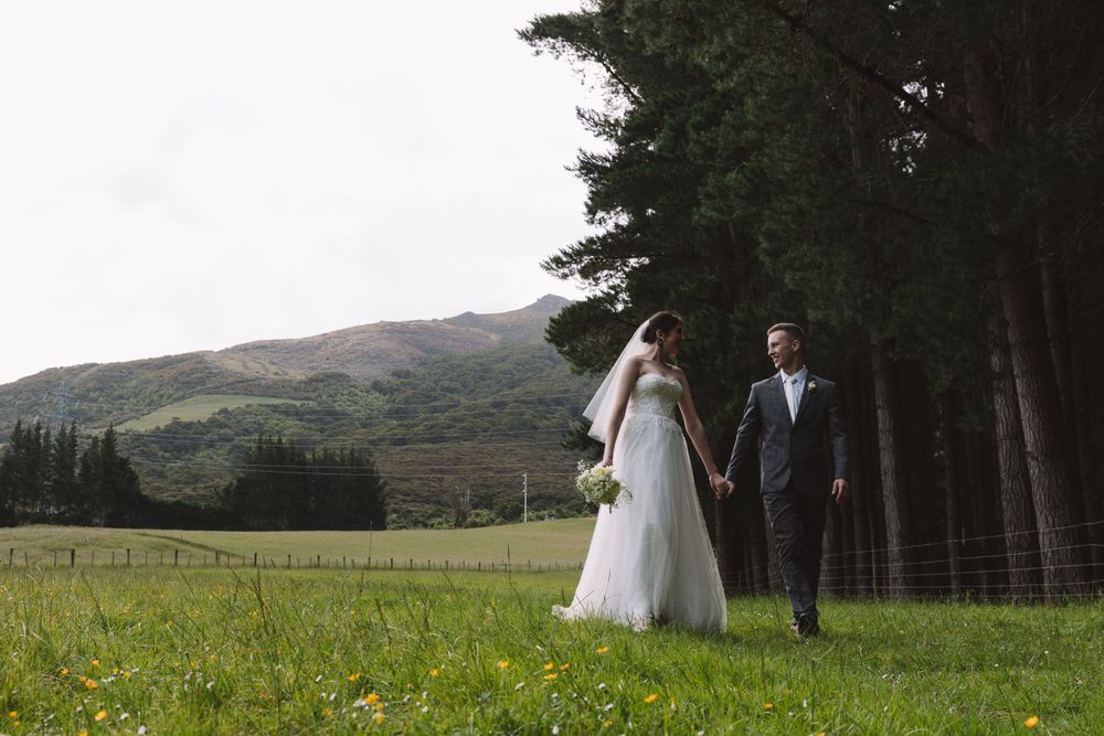 Bride and groom walk together through a mountain meadow alongside a forest of evergreens.