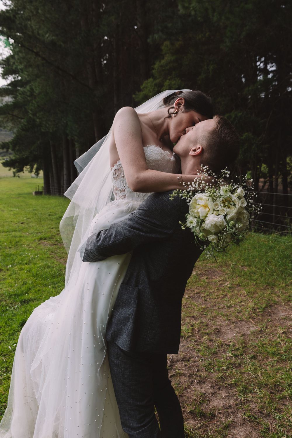 A tender wedding moment captured against a backdrop of evergreen trees and mountain scenery.