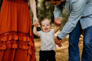 Joyful toddler holds hands with parents while walking on garden path.