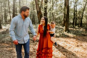 Family walks together through sunlit autumn forest with fallen leaves.