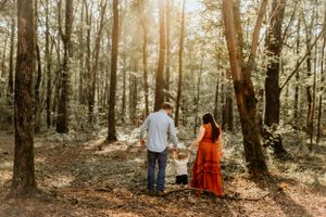 Family holds hands while walking through sunlit wooded area.