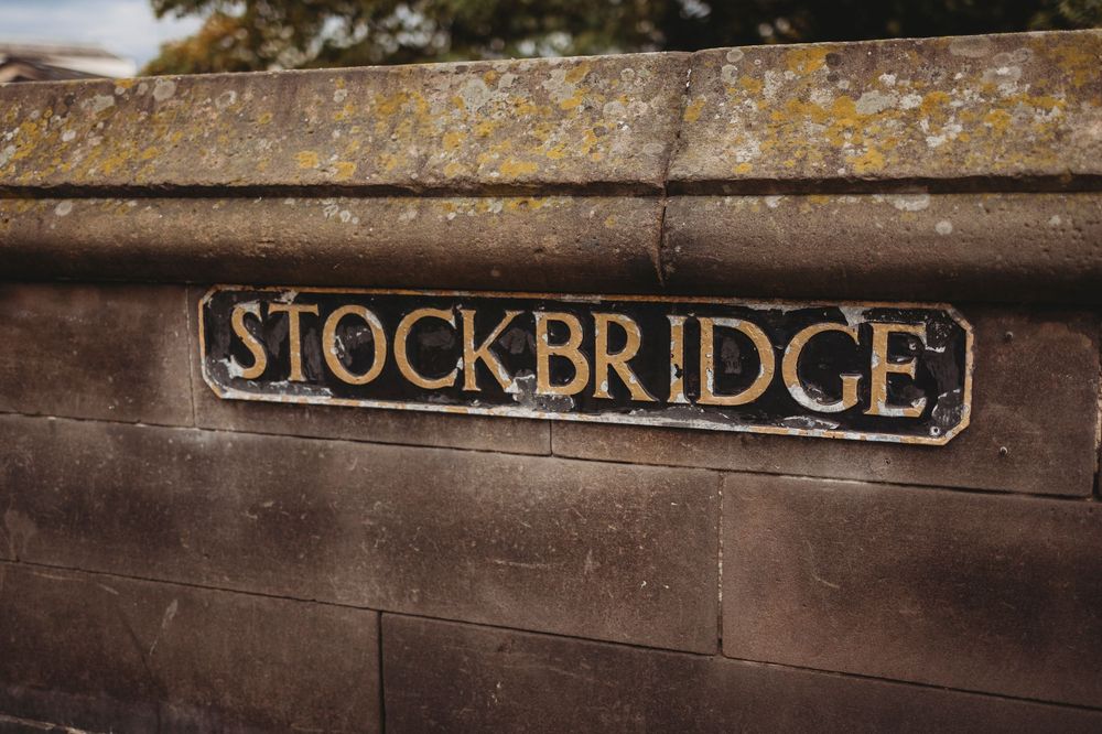 A weathered metal sign reading 'Stockbridge' mounted on an aged stone wall with patches of yellow lichen.