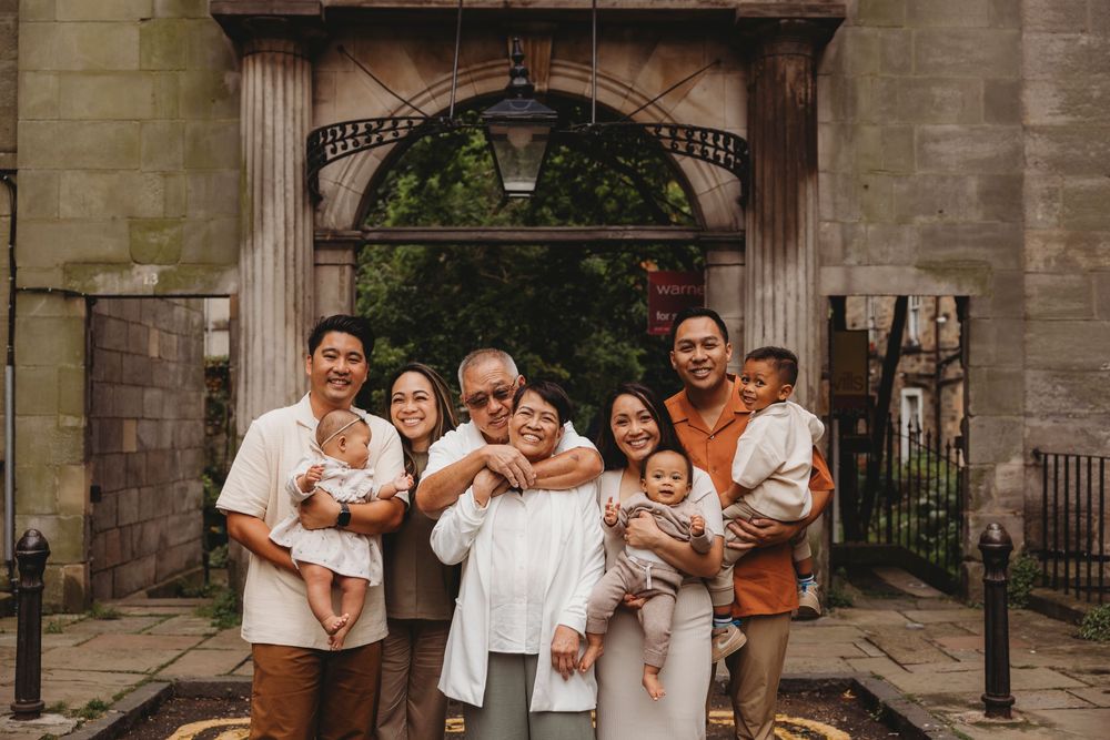 A group wearing coordinated white and beige outfits poses together in front of a stone archway entrance.