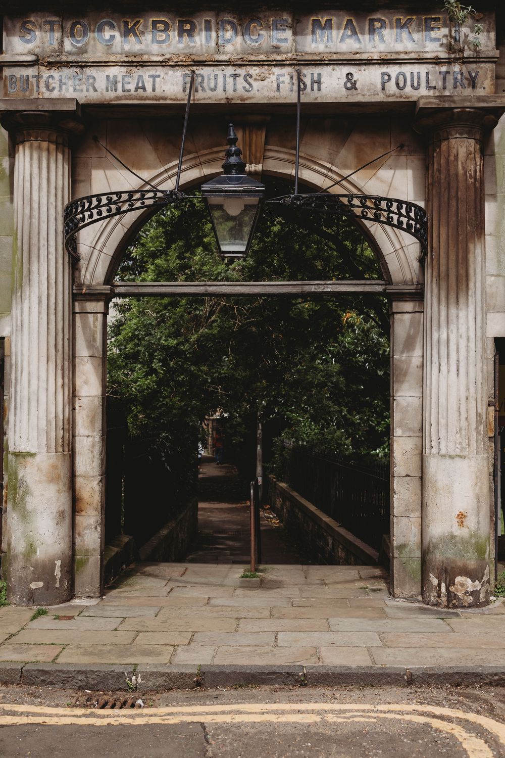 Historic stone archway entrance to Stockbridge Market with faded vintage signage for meat, fruits, fish and poultry in Edinburgh.