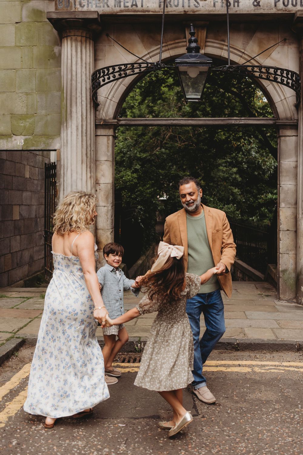 A family holds hands and dances together in a circle under a grand stone archway entrance.