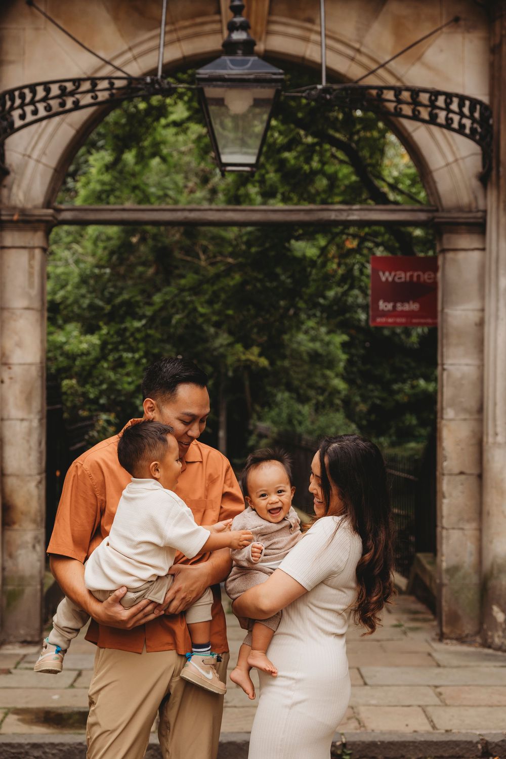 Family in warm-toned clothing stands beneath stone archway entrance with ornate metalwork and lantern.