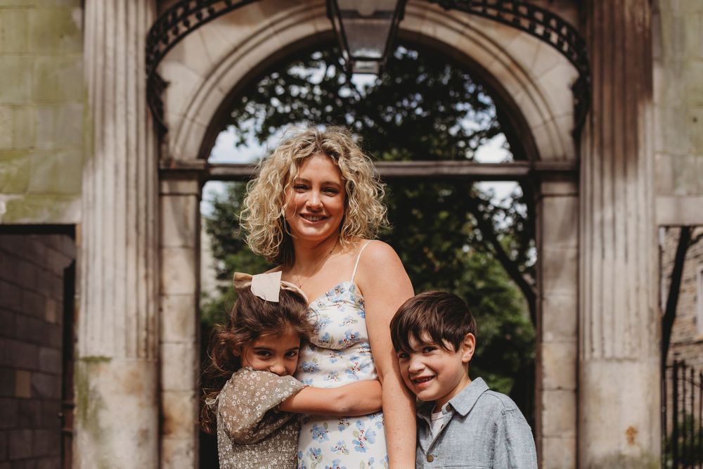 A family group stands smiling together under a grand stone archway at a historic building entrance.