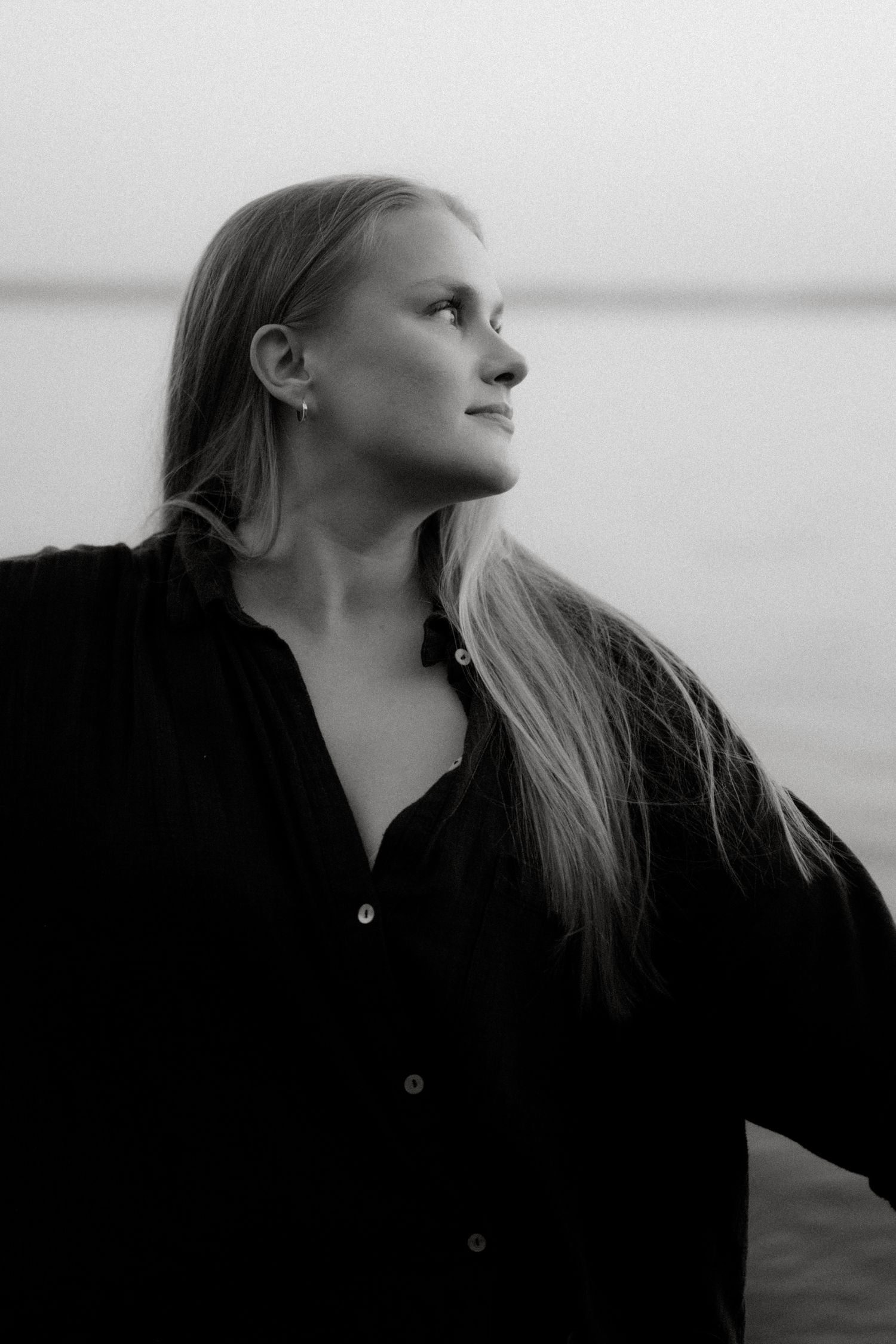 A side profile portrait of someone with flowing blonde hair gazing out over water at dusk.