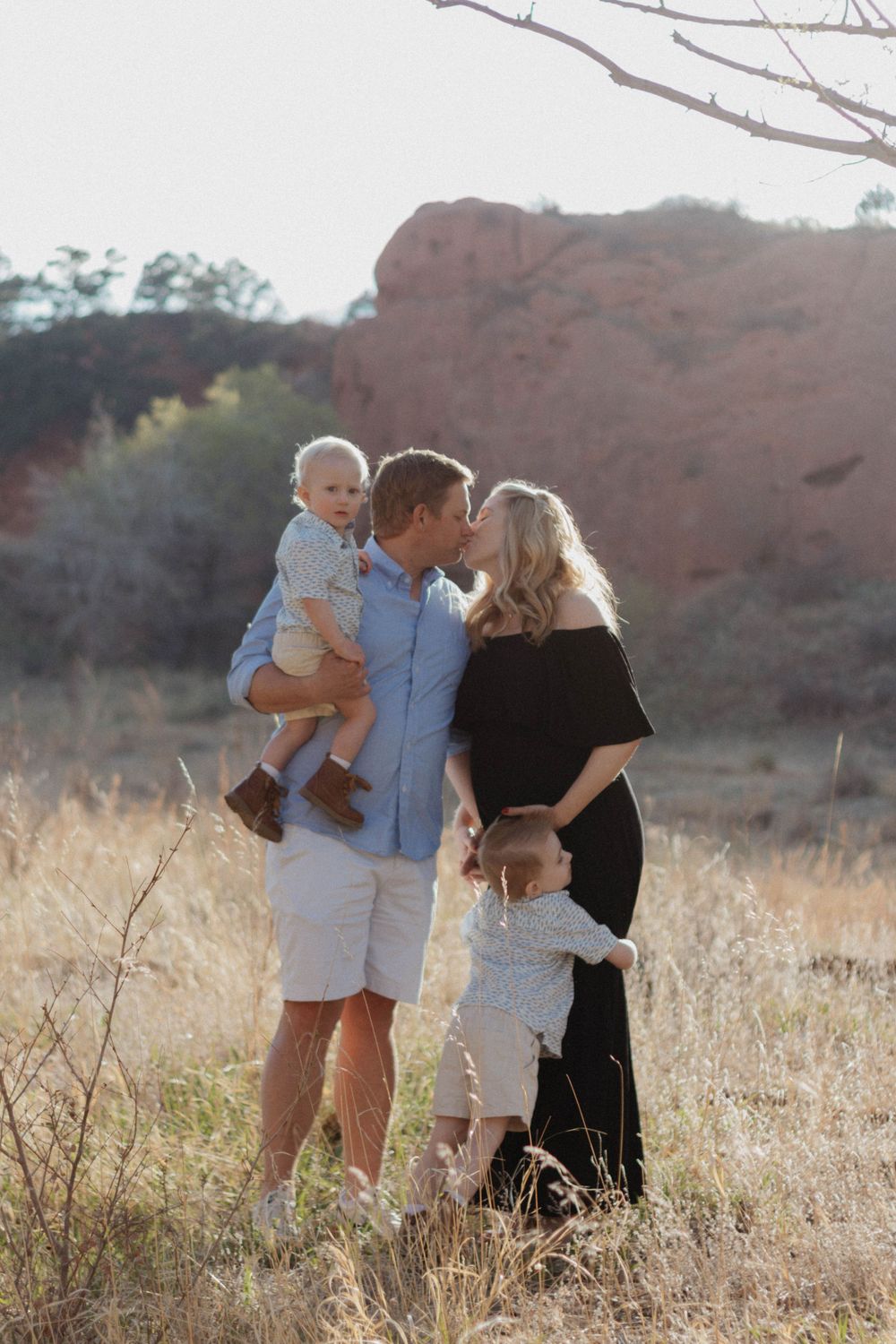 Sunset portrait of a family of four sharing an intimate moment in a field with red rocks in the background. Family photoshoot Colorado