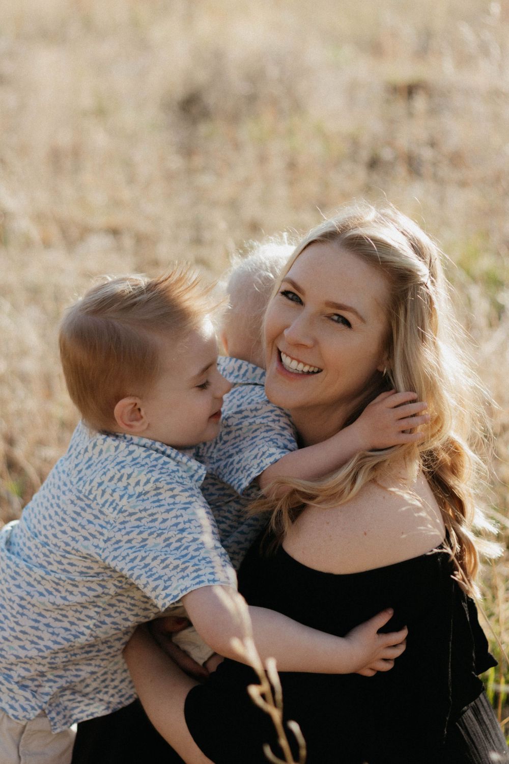 A heartwarming moment outdoors in a field with sunlit mother and child embracing and smiling together. Colorado's family photographer