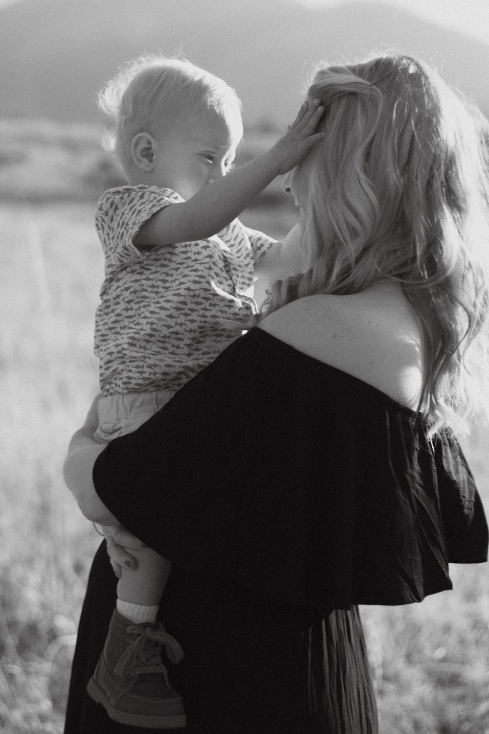 Black and white photo of a mother holding a small child in a field during a tender moment of connection. Mother photoshoot Colorado