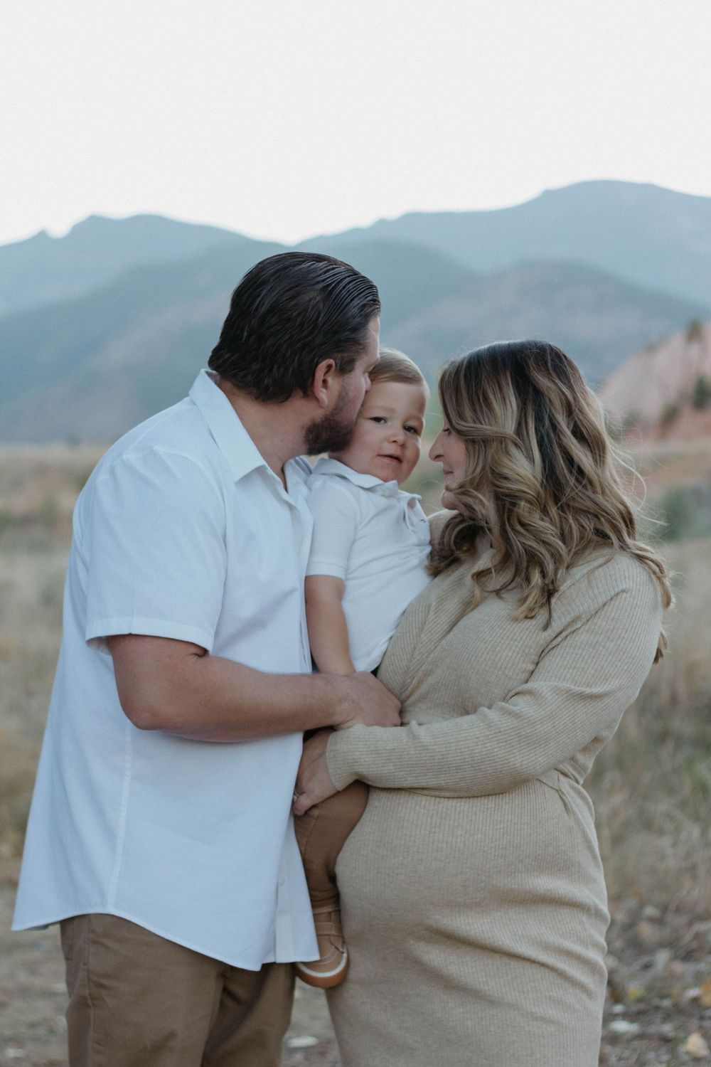family photoshoot in casual attire shares an intimate moment together against a mountainous backdrop at sunset in Colorado Springs, Colorado
