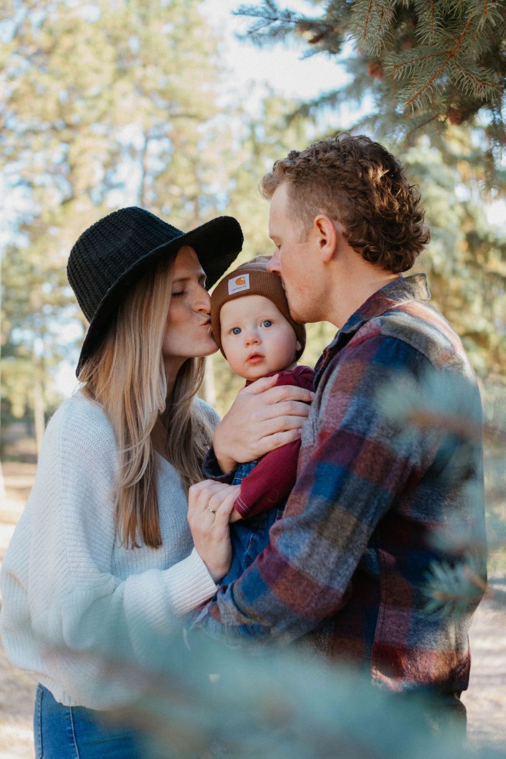 A family of three shares an intimate outdoor moment among pine trees on a sunny autumn day. family photoshoot in Colorado Springs, Colorado