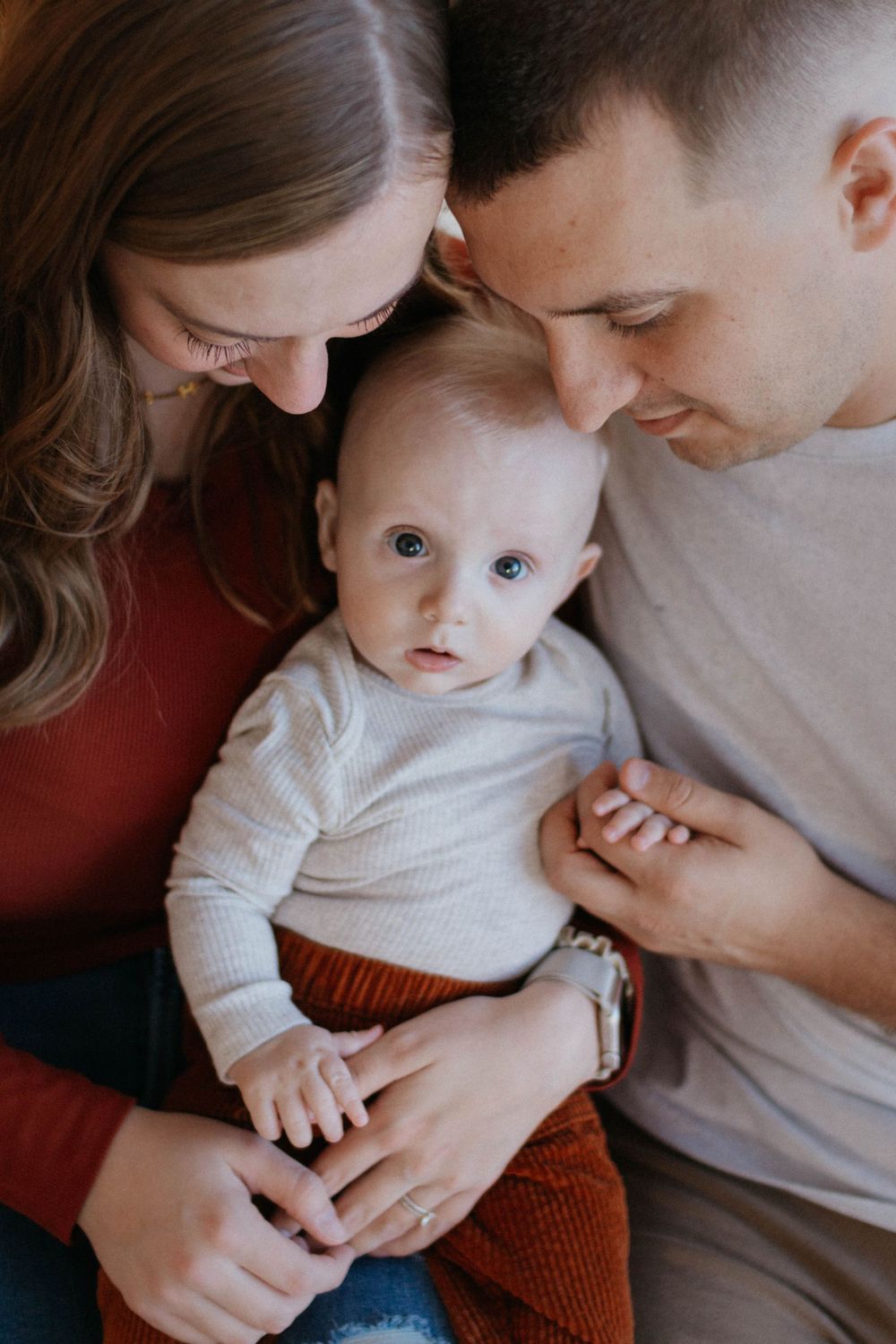 A baby in a white onesie and brown pants snuggles with their parents at holiday family photoshoot in a studio in Colorado