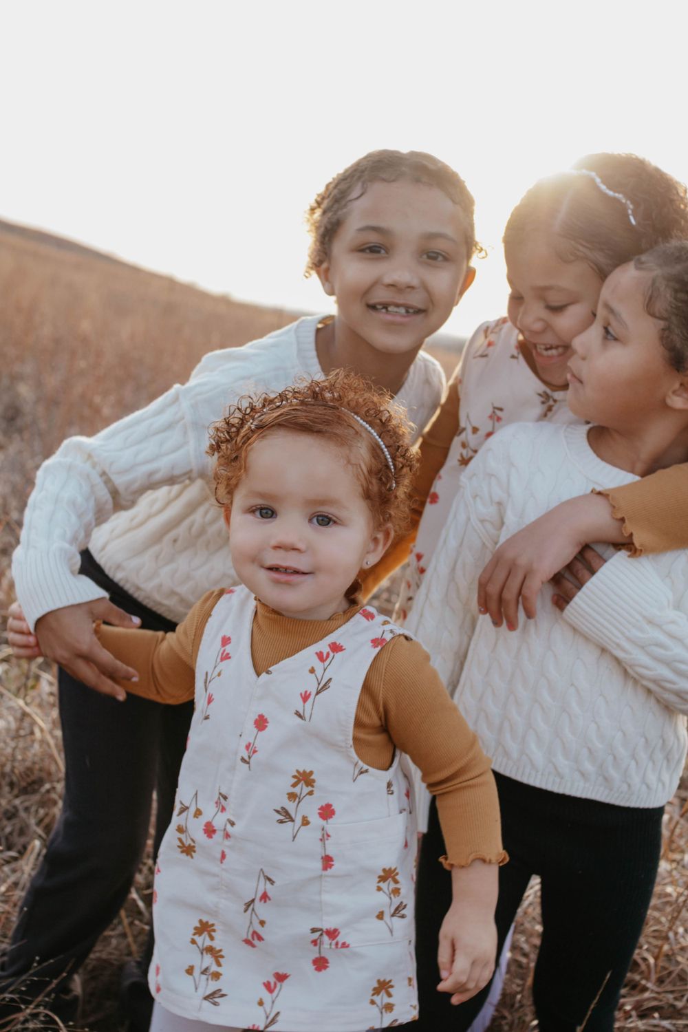 kids in sweaters and casual wear laugh together in a sunlit field during golden hour. family portraits, sisters, photoshoot. lifestyle
