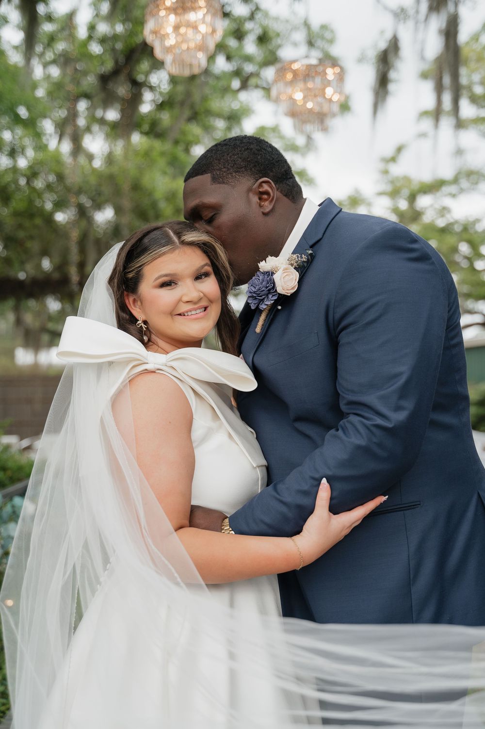 A happy couple shares an intimate moment during their outdoor garden wedding under crystal chandeliers.