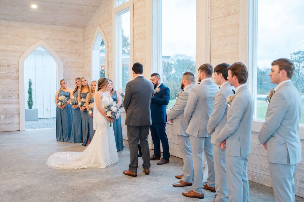 Wedding ceremony takes place in a bright chapel with bridesmaids in blue and groomsmen in gray suits.