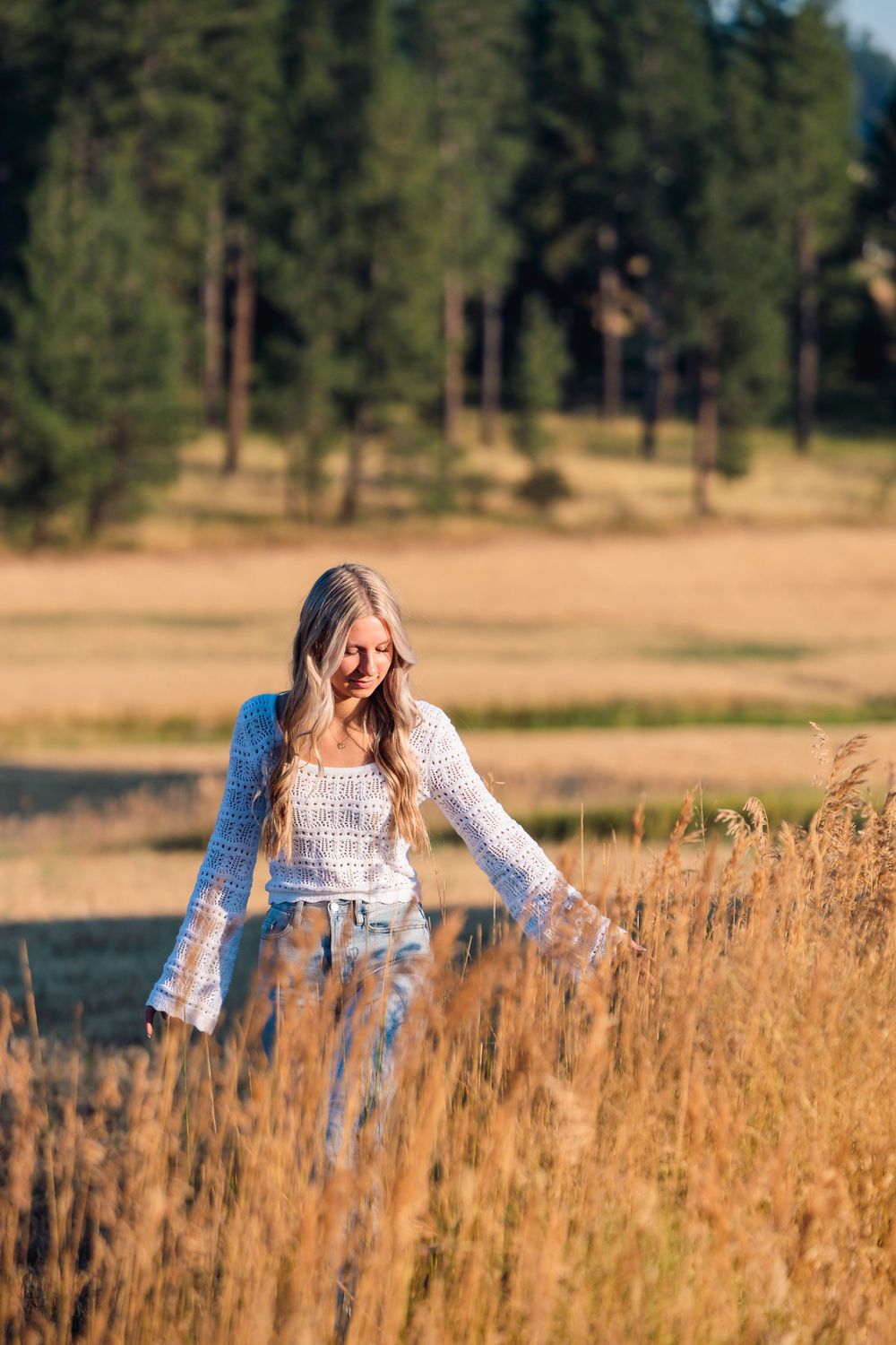 A woman in a white top and jeans strolls through tall grass during her senior session, capturing a moment of tranquility.