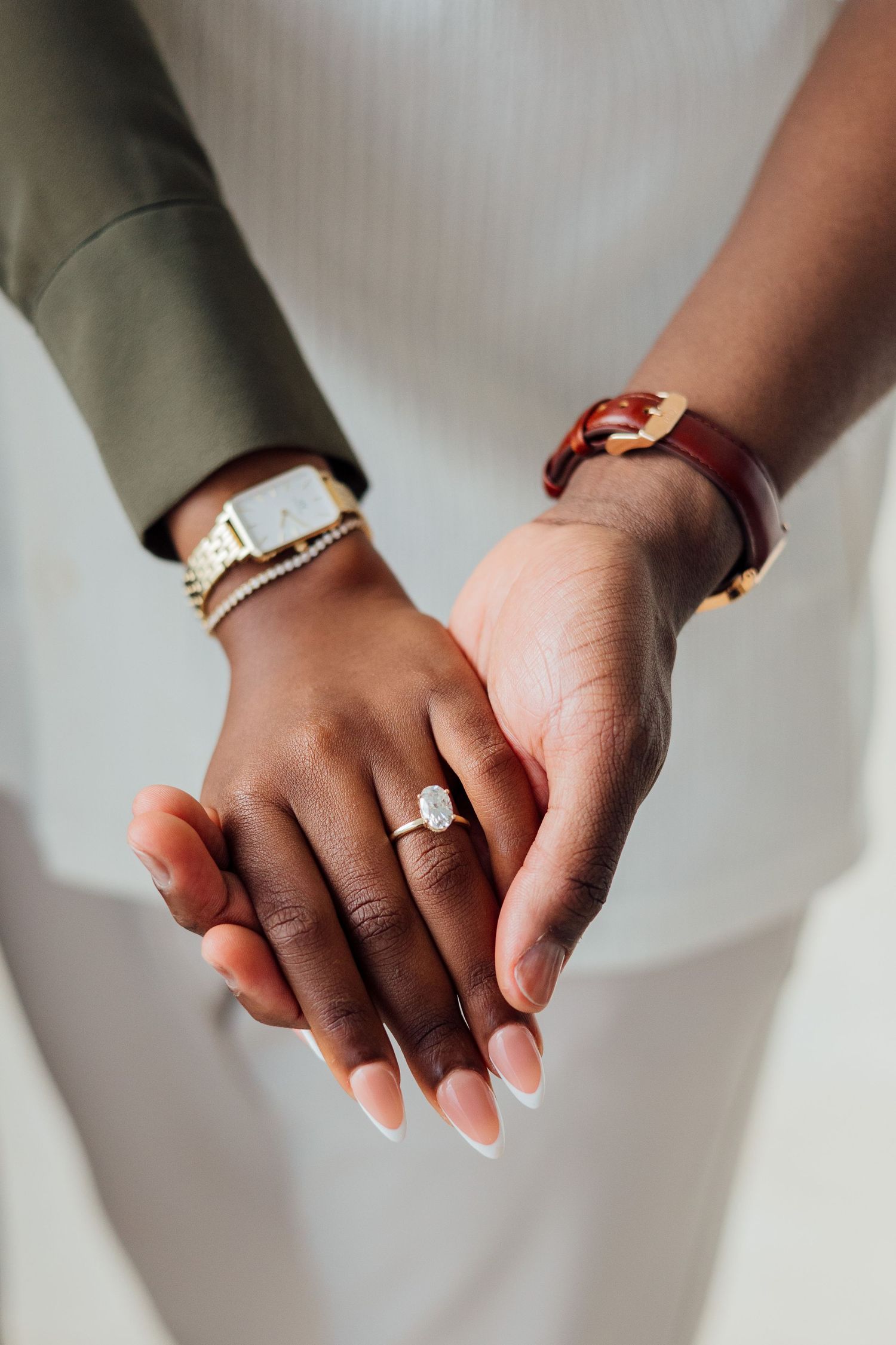 Close-up of hands wearing delicate jewelry including bracelets and an engagement ring against a white dress background.