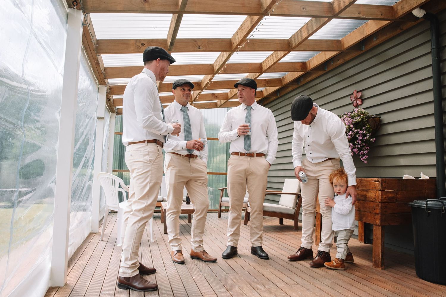 Groomsmen in light colored suits gathering on a wooden deck before the ceremony.