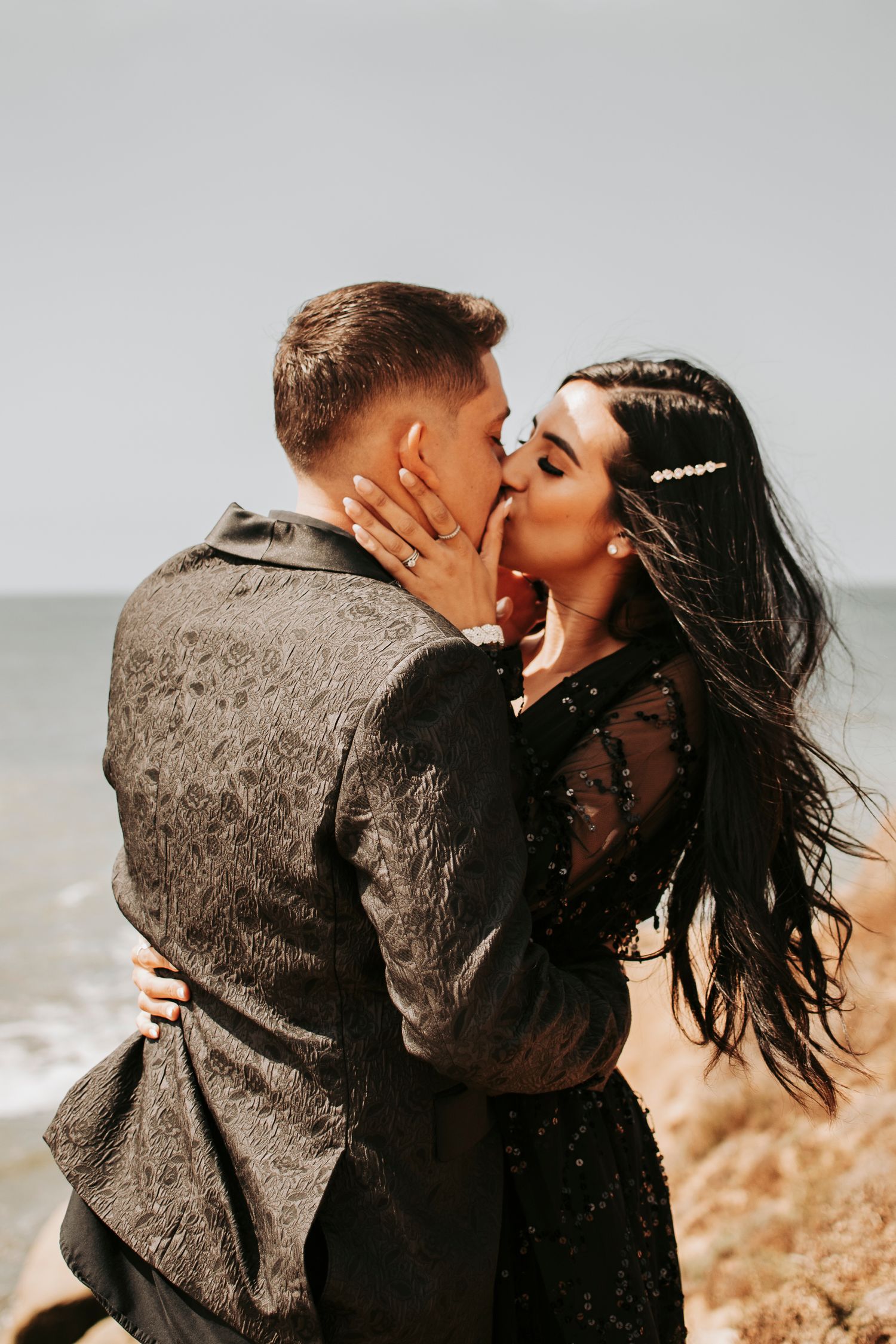 Romantic couple embracing and kissing on cliff overlooking ocean.