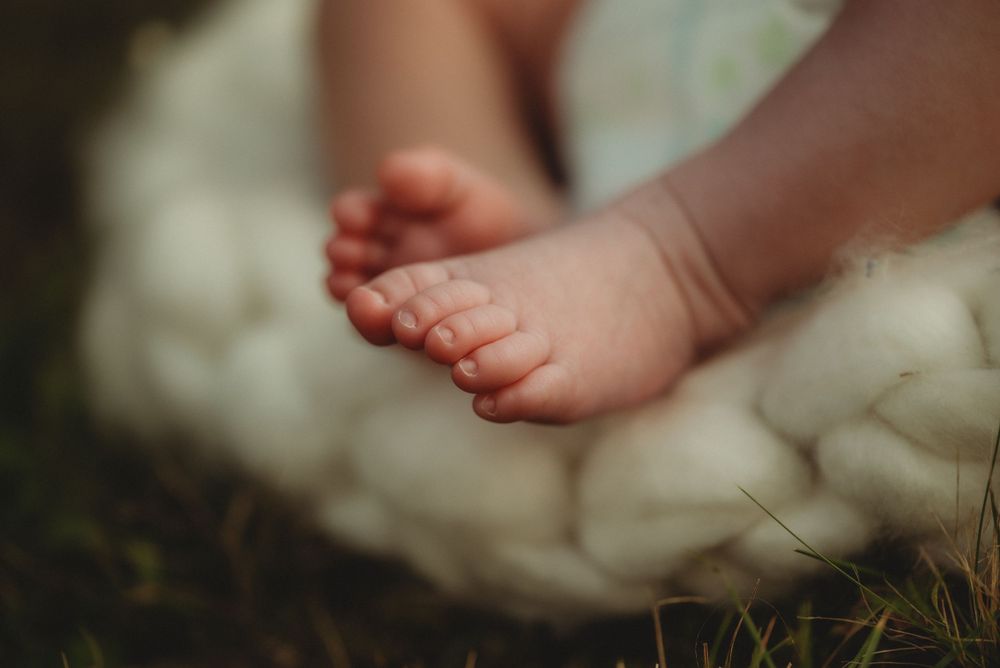 Close-up of tiny baby feet resting on soft white knitted blanket.