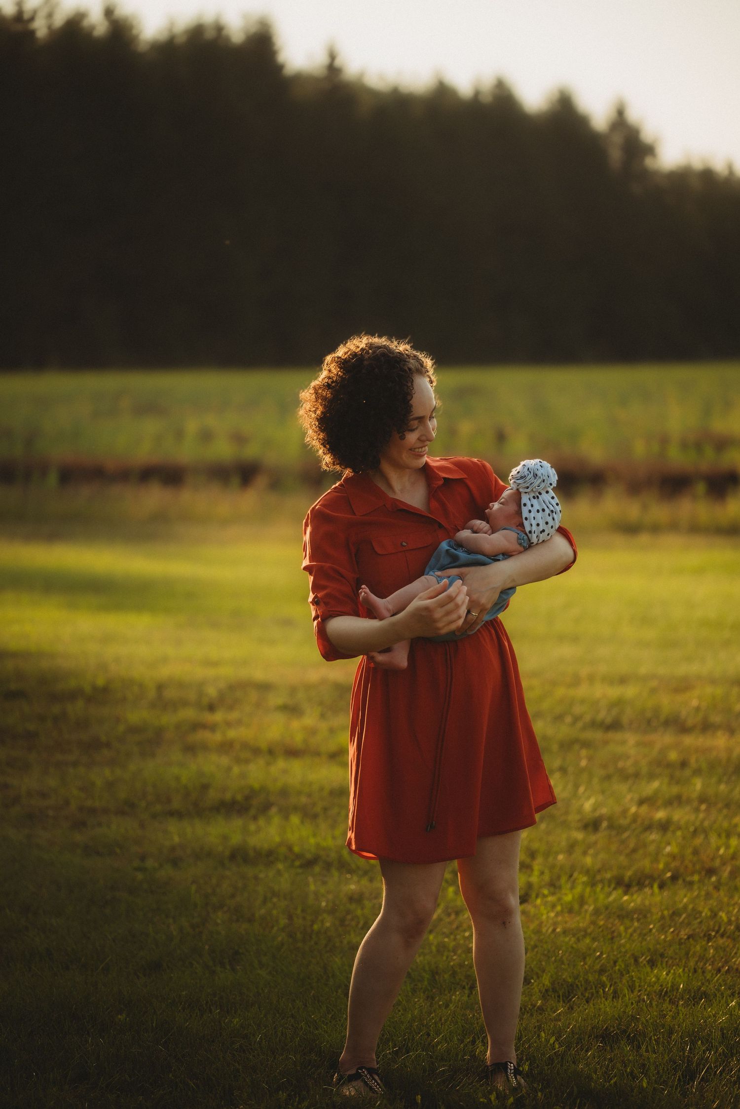 Person in red dress cradles an infant during golden hour in a grassy meadow.