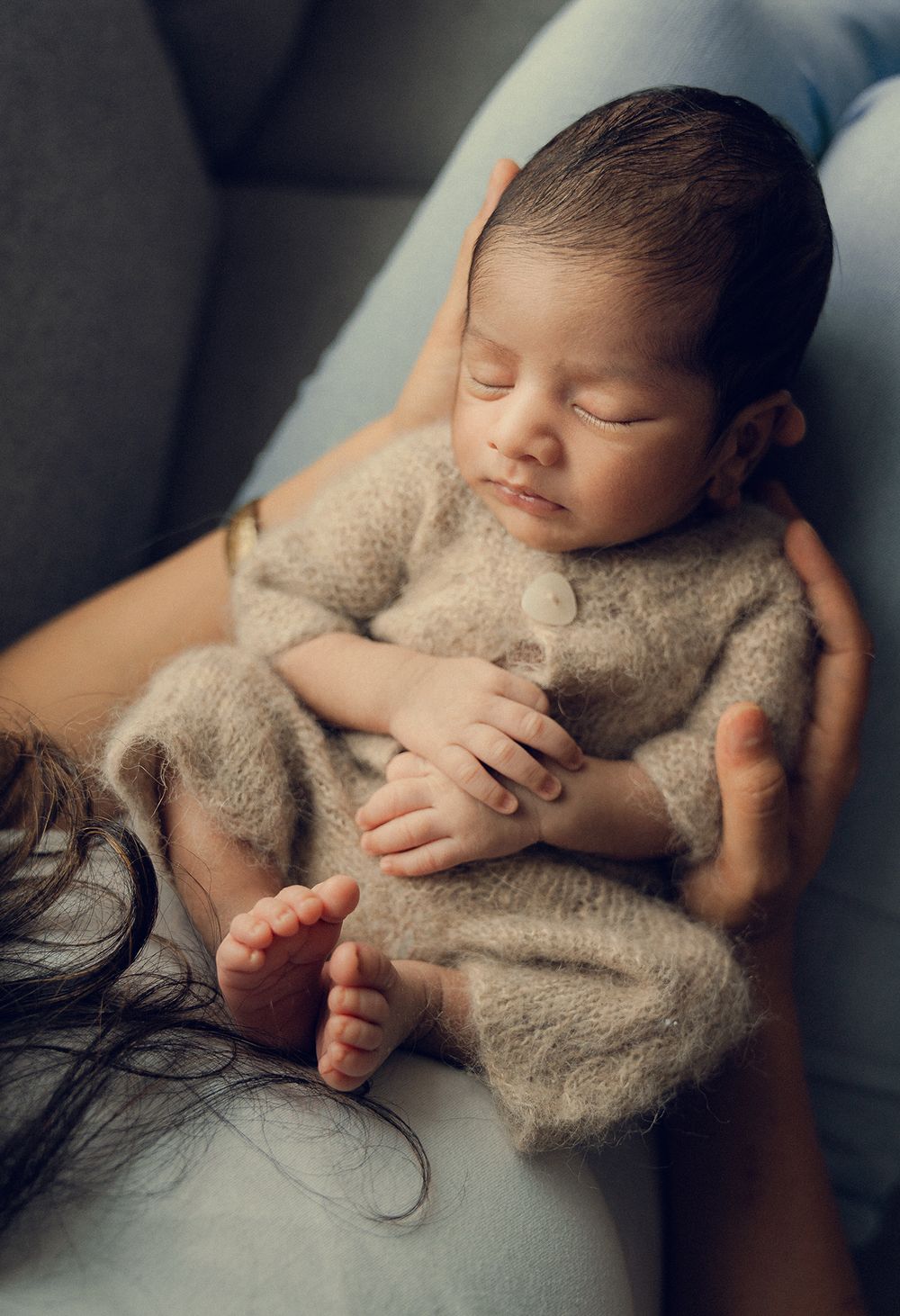 A sleeping newborn wrapped in a soft beige blanket lies peacefully against a dark background in a series of gentle poses.