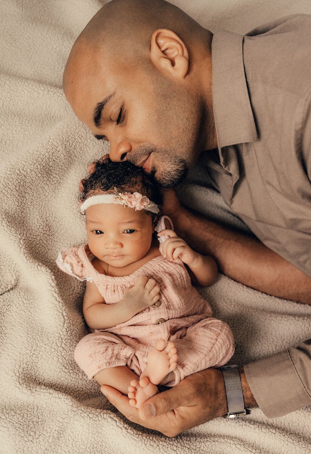 A tender moment showing parent cradling newborn baby wearing pink onesie on beige blanket.