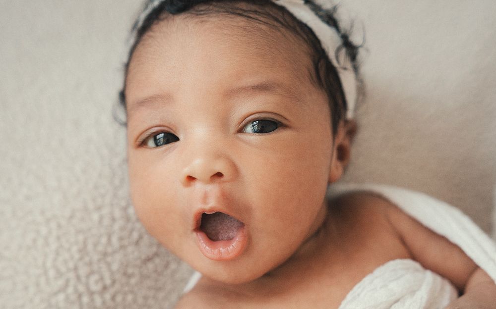 A collection of four close-up photos showing an adorable newborn baby lying on a light gray blanket.