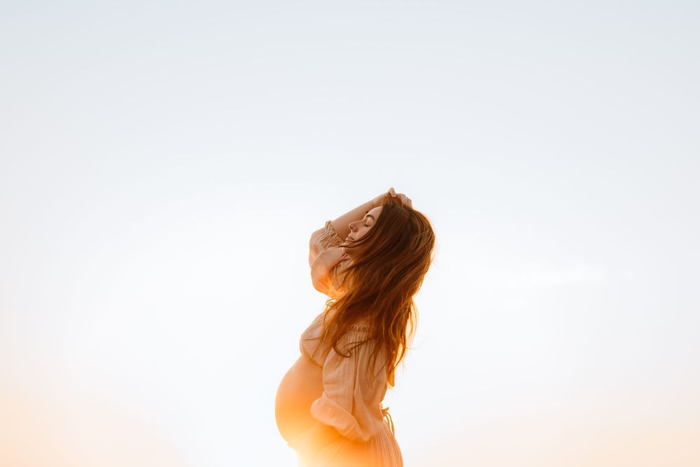 Silhouette of a woman with flowing hair backlit by golden sunlight during sunset. Natural maternity photos sydney. Pregnancy photos.