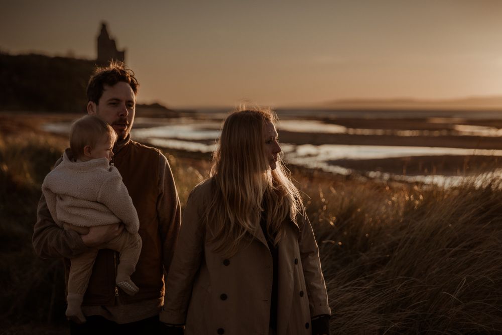 couple walking by the beach at sunset while the dad hols their toddler