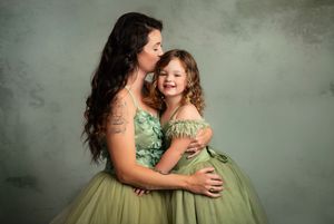 Mother and daughter wearing matching green dresses embrace and laugh during a studio photo session.