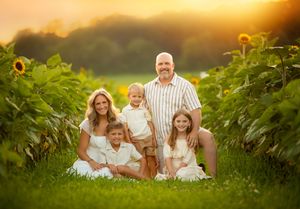 A group in white clothes sits together among sunflower plants during a warm golden sunset.