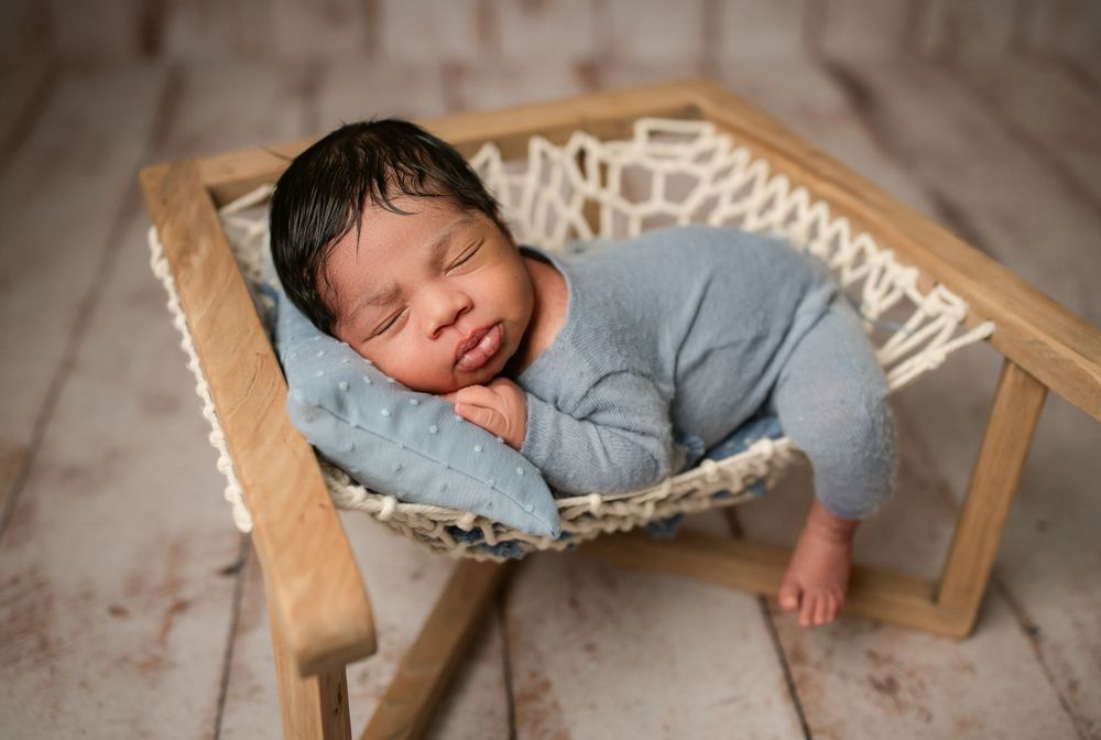 Peaceful newborn sleeping in a hammock wearing light blue sleepwear during professional photo session.