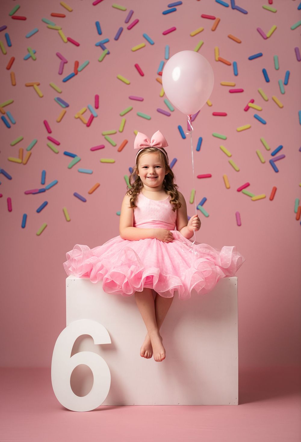 A sweet birthday portrait series showing a pink party dress against a pink backdrop with confetti and white number 6 prop.