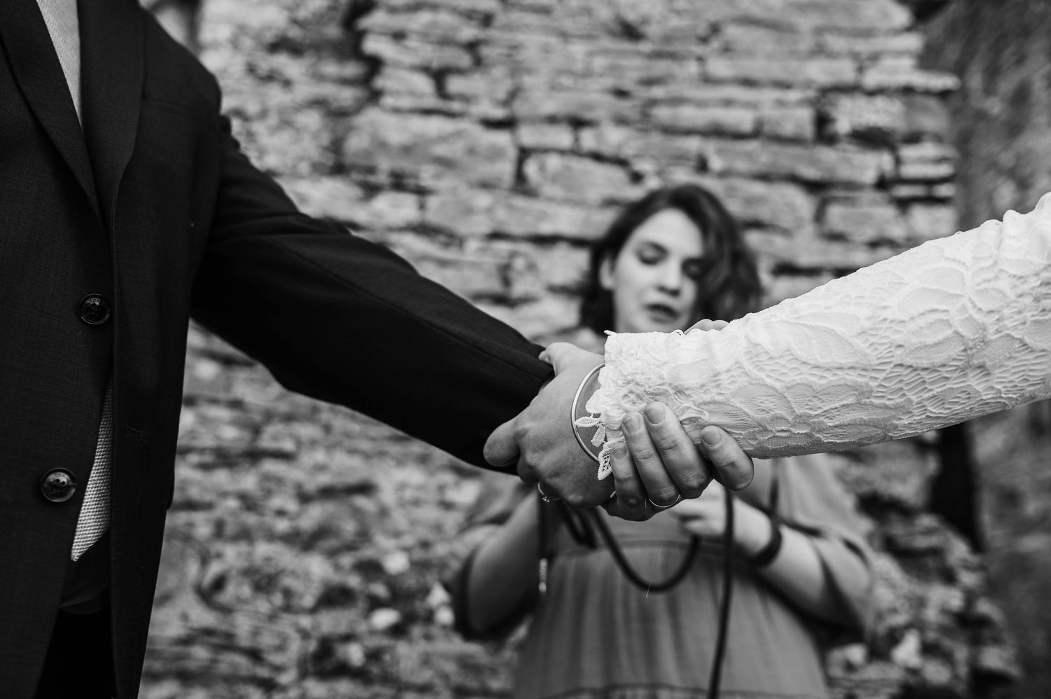 A black and white photo capturing hands clasped in a romantic moment with a stone wall in the background.