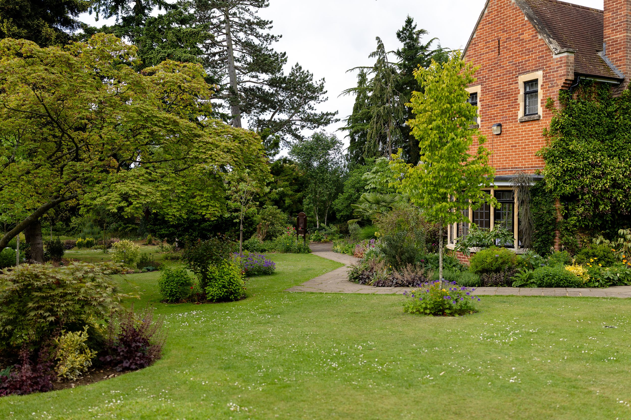 Elegant brick building with glass conservatory and manicured garden terrace featuring outdoor seating and landscaped grounds.