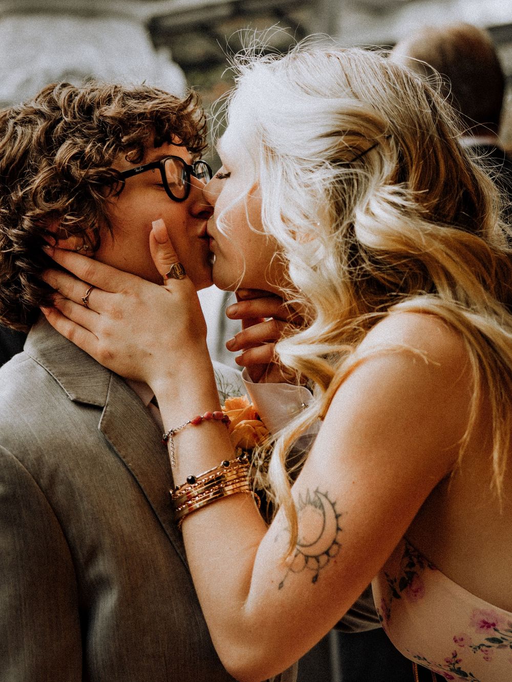 A romantic close-up of a couple sharing an intimate kiss, with blonde hair and a visible arm tattoo.