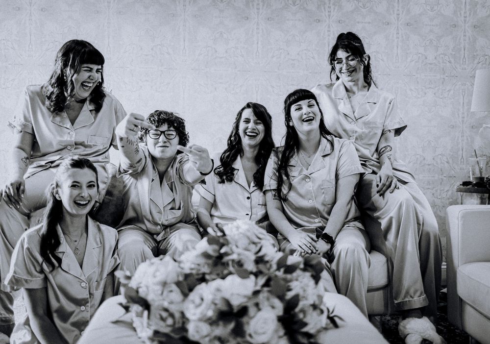 A black and white photo shows a group sitting together on a sofa with flowers in the foreground.
