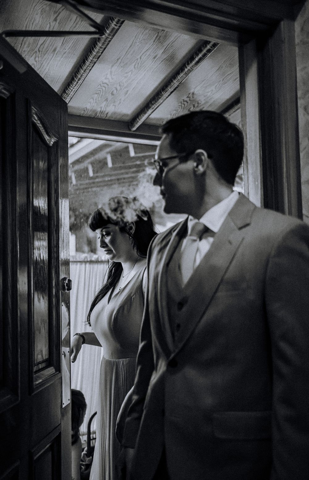 Black and white photograph of a couple in formal attire standing in an ornate doorway at a wedding.