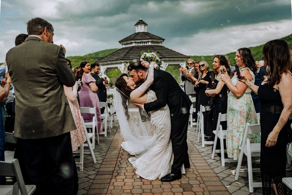 A romantic wedding ceremony takes place on an outdoor deck with a gazebo and guests watching from white chairs.