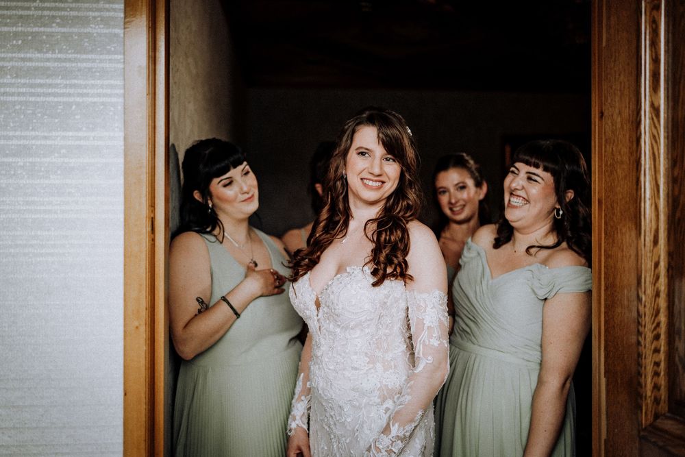 A bride in white lace poses with three bridesmaids in soft mint green dresses while sharing joyful laughter together.