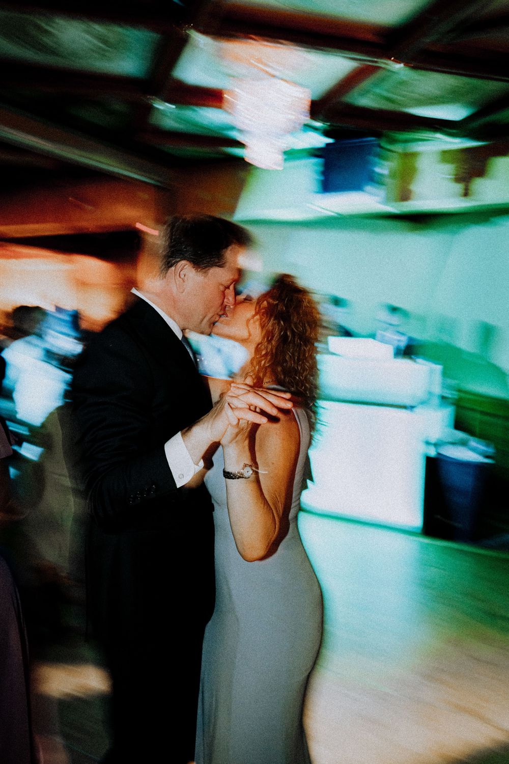 A couple shares a romantic dance moment in a dimly lit room with blurred motion and colorful lighting effects.