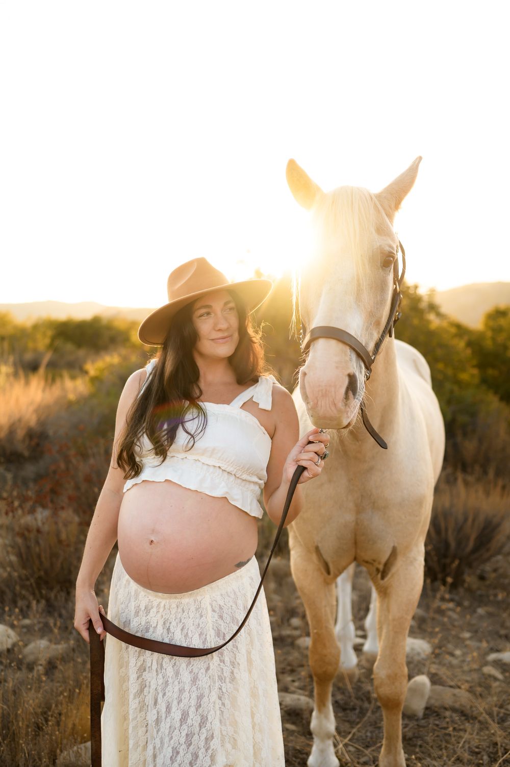 woman and white horse stand face to face in sunlight at Ojai Valley Trail riding during her maternity photoshoot in Ojai