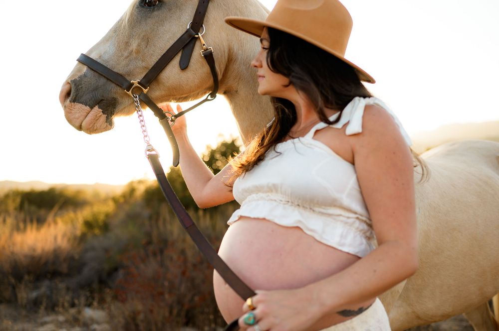 woman holds horse rein in cowboy outfit during her maternity photoshoot in Ojai river preserve at Ojai Valley Trial Riding Company