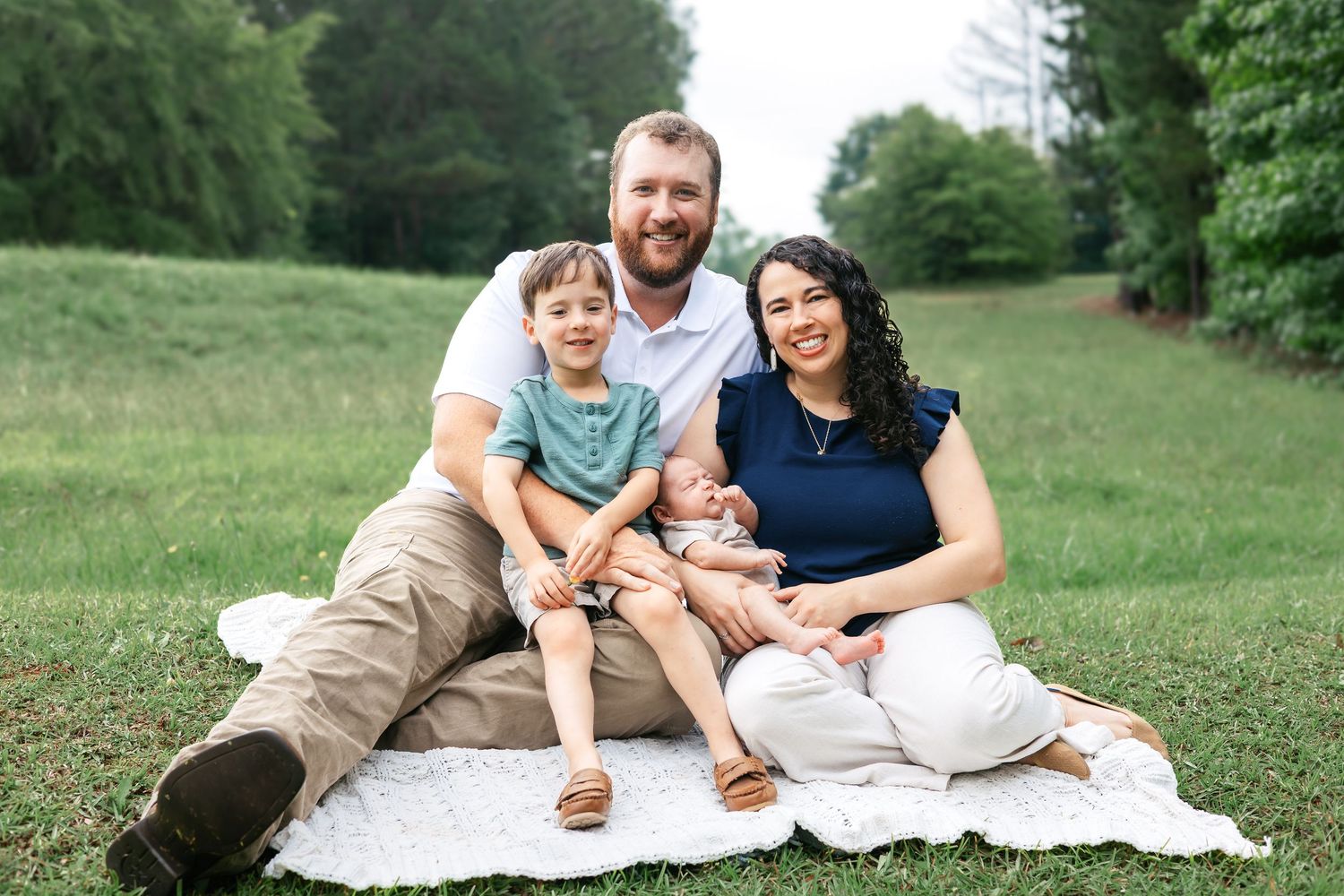 Family of four smile together in the grass holding new baby boy during outdoor newborn session in Athens, GA.