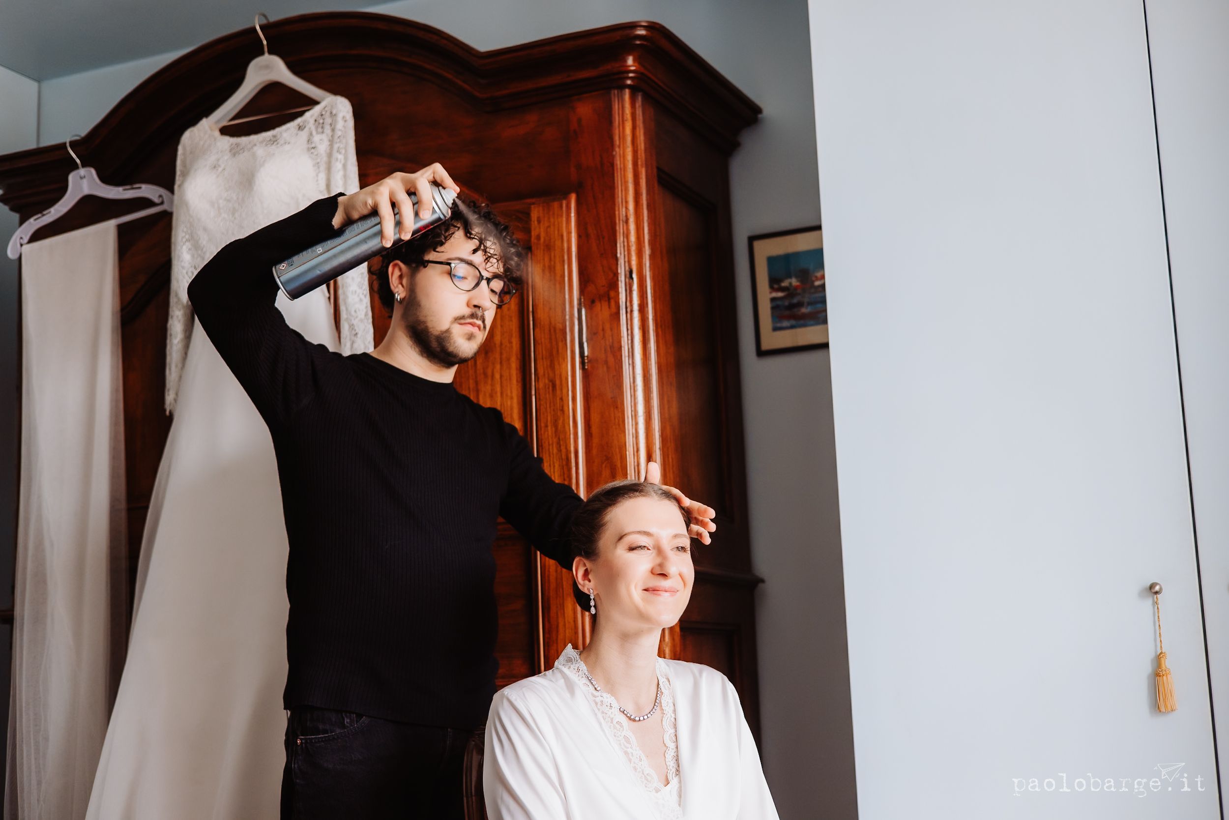 Wedding day preparation scene with a hairstylist styling a bride's hair in a cozy home setting.