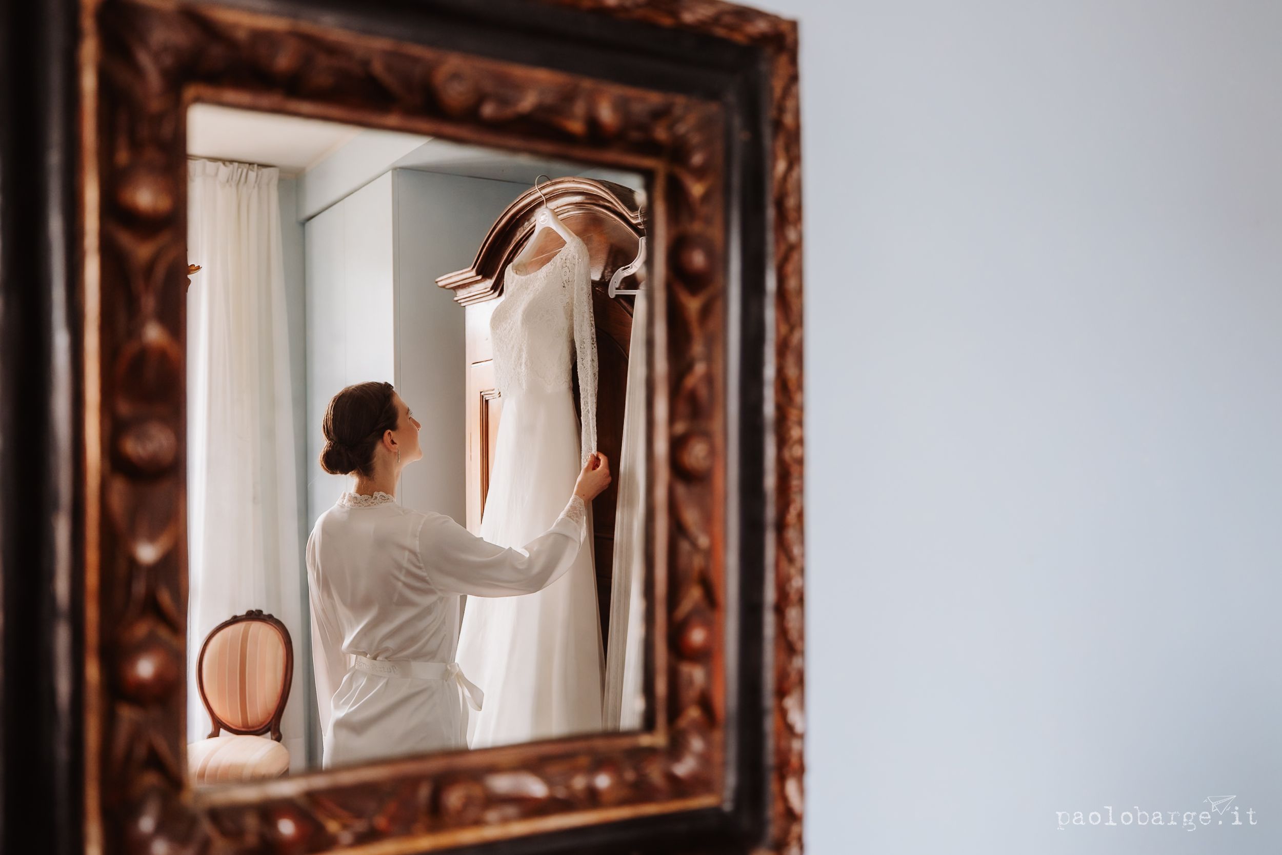 Ornate brown wooden frames hang on a white wall showing reflections of sunlight from a nearby window.