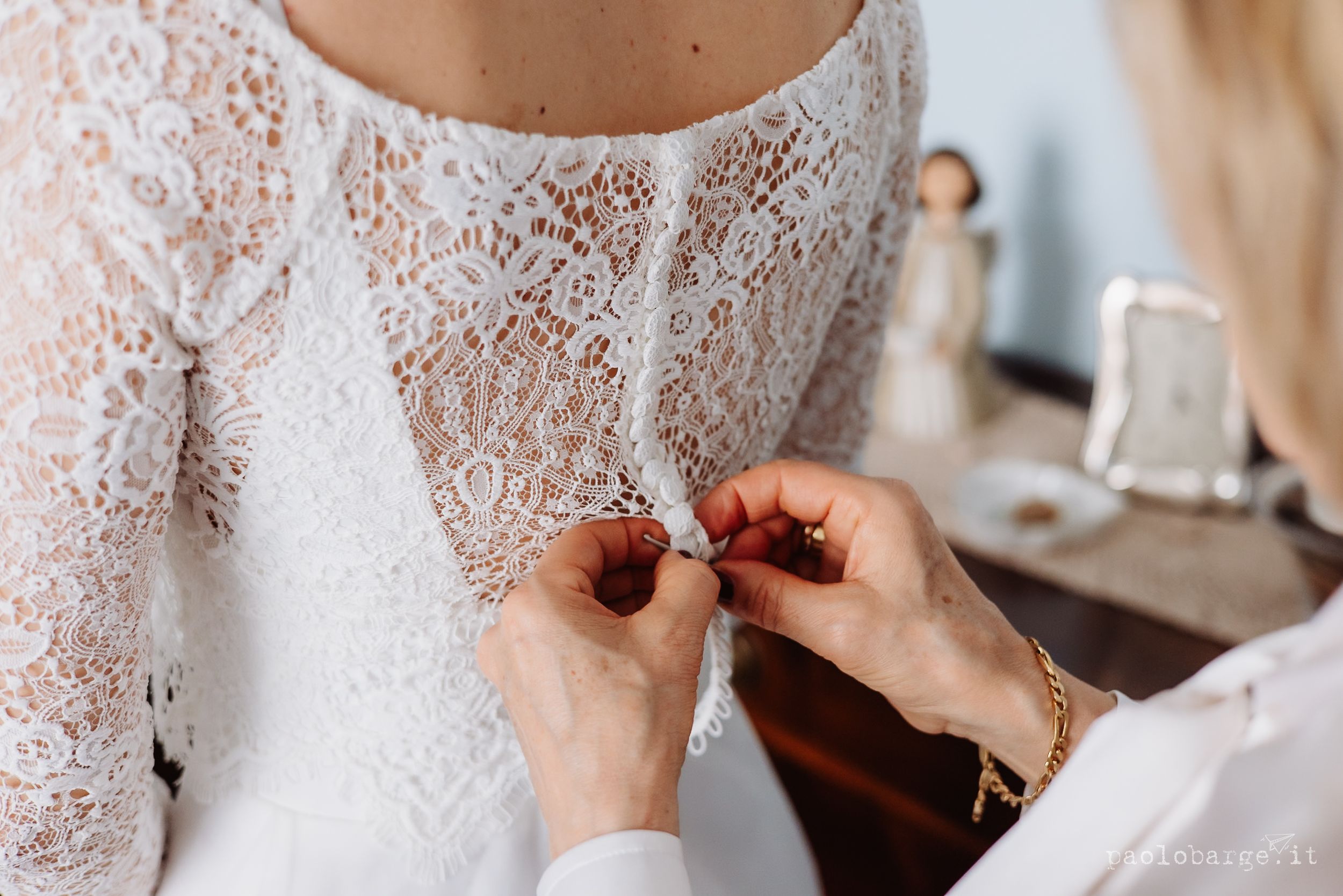 Close-up of hands adjusting delicate white lace details on an elegant wedding dress during final fitting preparations.